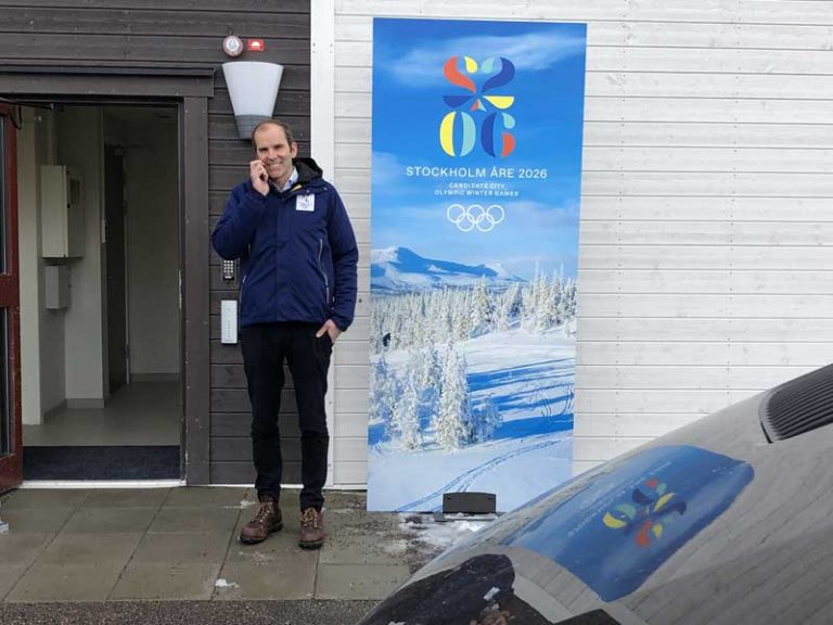 Stockholm-Åre 2026 CEO Richard Brisius stands beside bid banner at side-entrance to Lugnet Nordic Complex in Falun, Sweden March 14, 2019. It was a rare appearance of promotional material in Sweden (GamesBids Photo)